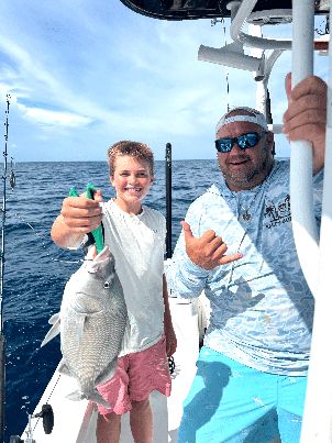 Two anglers giving a thumbs-up with a fresh catch offshore